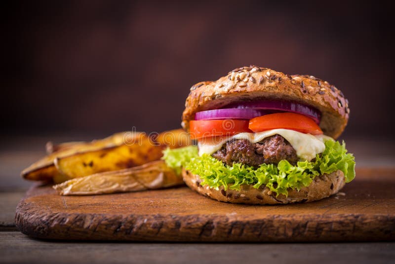 Home made hamburger with green salad and with american potatoes behind. Brown wooden background