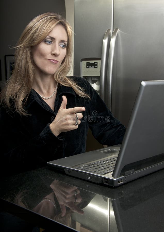 Woman sitting in front of laptop at black granite island pointing finger like gun. Woman sitting in front of laptop at black granite island pointing finger like gun