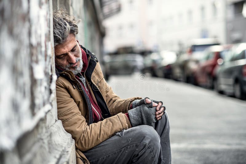 Homeless beggar man sitting outdoors in city asking for money donation, sleeping.