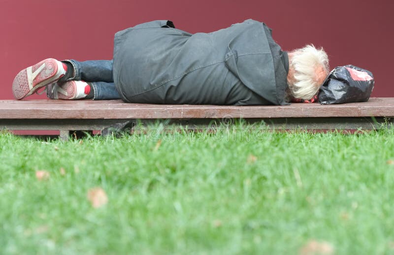Bezdomovec ležící na lavičce.
