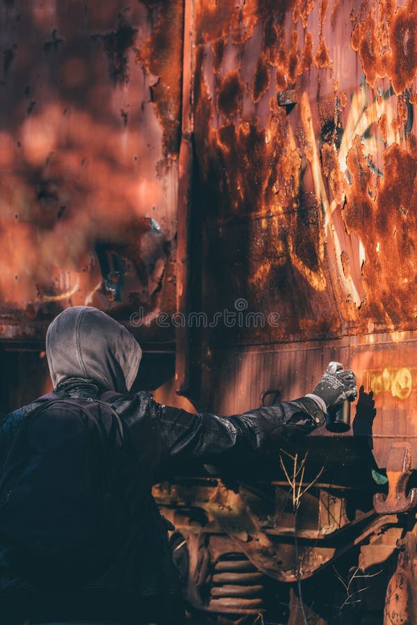 Homeless man spray painting old train wagon with aerosol can. Unrecognizable male person in conceptual image with selective focus