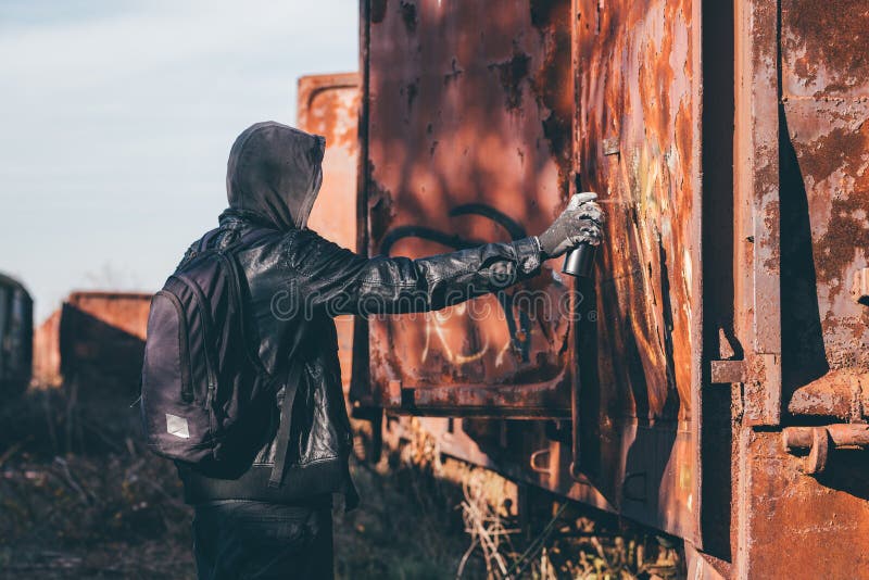 Homeless man spray painting old train wagon with aerosol can. Unrecognizable male person in conceptual image with selective focus