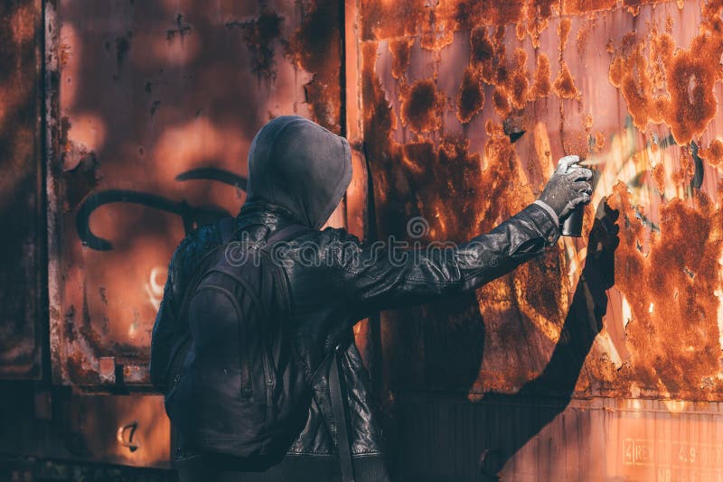 Homeless man spray painting old train wagon with aerosol can. Unrecognizable male person in conceptual image with selective focus