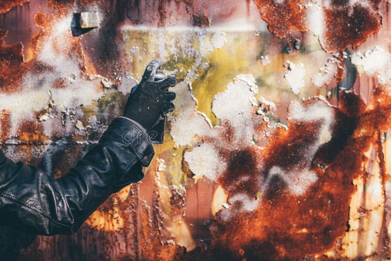 Homeless man spray painting old train wagon with aerosol can. Unrecognizable male person hand close up in conceptual image with selective focus
