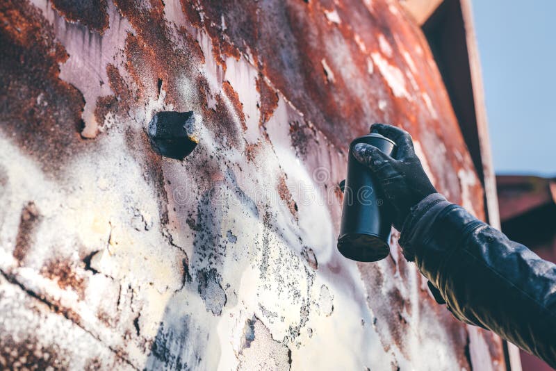 Homeless man spray painting old train wagon with aerosol can. Unrecognizable male person hand close up in conceptual image with selective focus