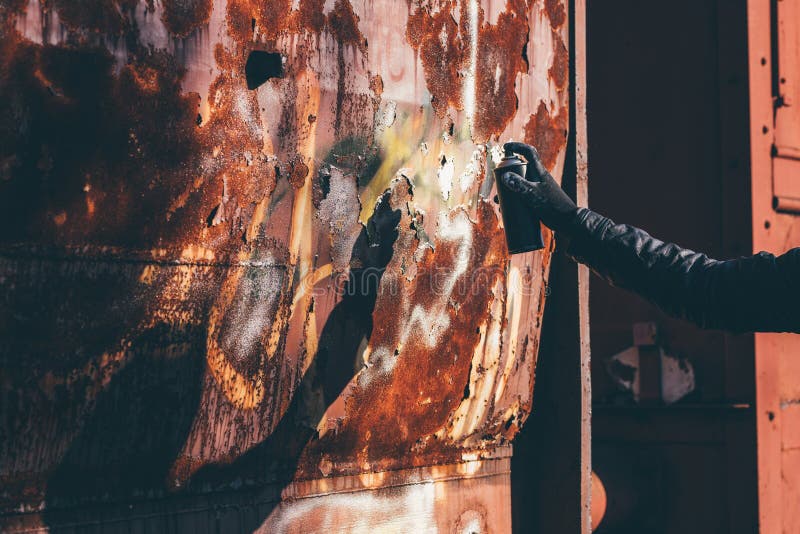 Homeless man spray painting old train wagon with aerosol can. Unrecognizable male person hand close up in conceptual image with selective focus