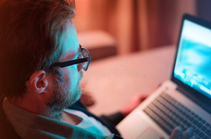 Homem adulto que trabalha na noite no laptop em casa imagens de stock Homem adulto que trabalha na noite no laptop em casa imagens de stock