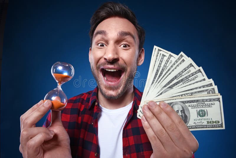 Homem afortunado que guarda o dinheiro e a ampulheta de 100 notas de dólar em sua mão fotografia de stock royalty free Homem afortunado que guarda o dinheiro e a ampulheta de 100 notas de dólar em sua mão fotografia de stock royalty free