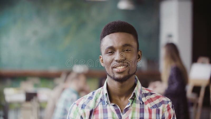 Homem africano considerável no escritório moderno ocupado Retrato do homem bem sucedido novo que olha a câmera e o sorriso