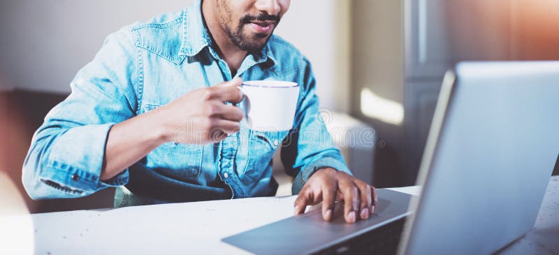 Homem africano novo de sorriso que faz a conversação video através do portátil com sócios ao beber o chá preto do copo branco den fotos de stock royalty free Homem africano novo de sorriso que faz a conversação video através do portátil com sócios ao beber o chá preto do copo branco den fotos de stock royalty free