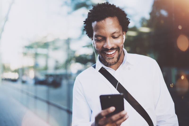 Homem afro-americano novo feliz no fones de ouvido que anda na cidade ensolarada e que faz a conversação video com os amigos no s fotos de stock royalty free Homem afro-americano novo feliz no fones de ouvido que anda na cidade ensolarada e que faz a conversação video com os amigos no s fotos de stock royalty free