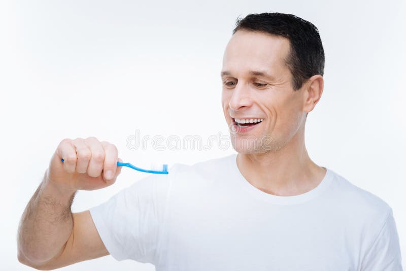 Homem agradável deleitado que olha sua escova de dentes imagem de stock Homem agradável deleitado que olha sua escova de dentes imagem de stock
