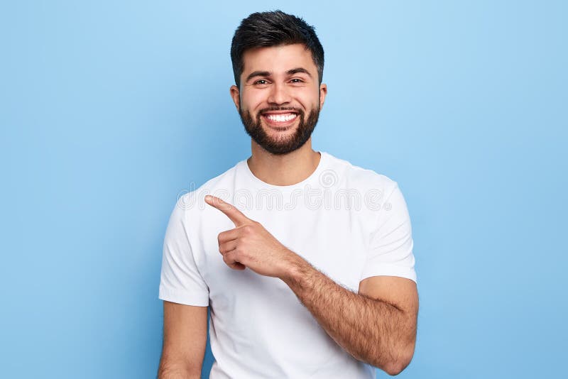 Homem alegre considerável novo que aponta, isolado no fundo azul imagem de stock royalty free Homem alegre considerável novo que aponta, isolado no fundo azul imagem de stock royalty free