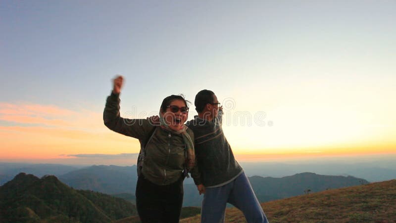 Homem alegre e mulher asiáticos que relaxam sobre o céu bonito do por do sol do agaisnt da montanha