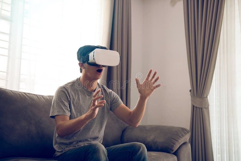 Homem asi?tico novo que veste vidros da realidade virtual na sala de visitas para admirar a realidade virtual imagem de stock royalty free Homem asi?tico novo que veste vidros da realidade virtual na sala de visitas para admirar a realidade virtual imagem de stock royalty free