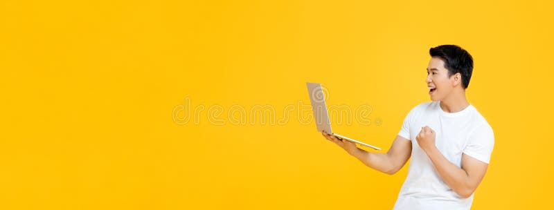 Homem asiático feliz transportando computador portátil e levantando o punho fazendo sim, isolado em fundo de faixa amarela com