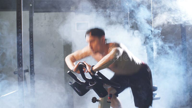 Homem atlÃ©tico branco forte treinando sem camisa em um simulador de bicicleta na academia