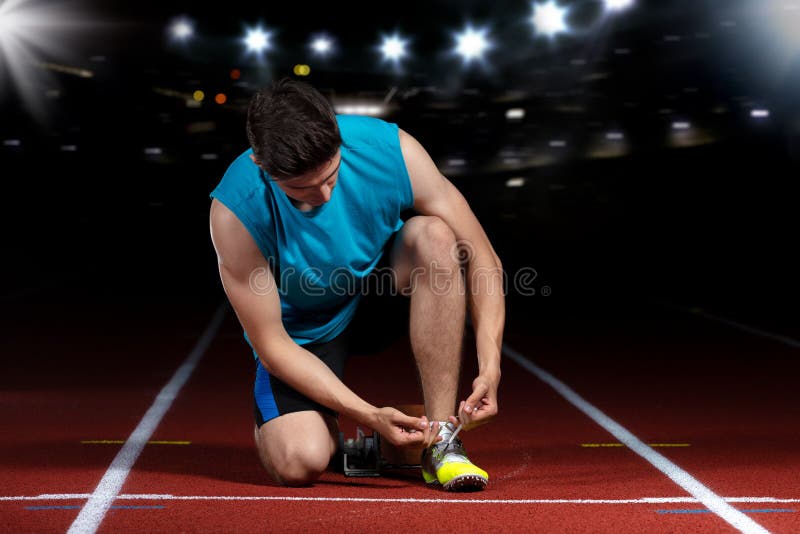 Homem atlético novo que senta-se na pista de atletismo e que estica no estádio dos esportes imagens de stock Homem atlético novo que senta-se na pista de atletismo e que estica no estádio dos esportes imagens de stock