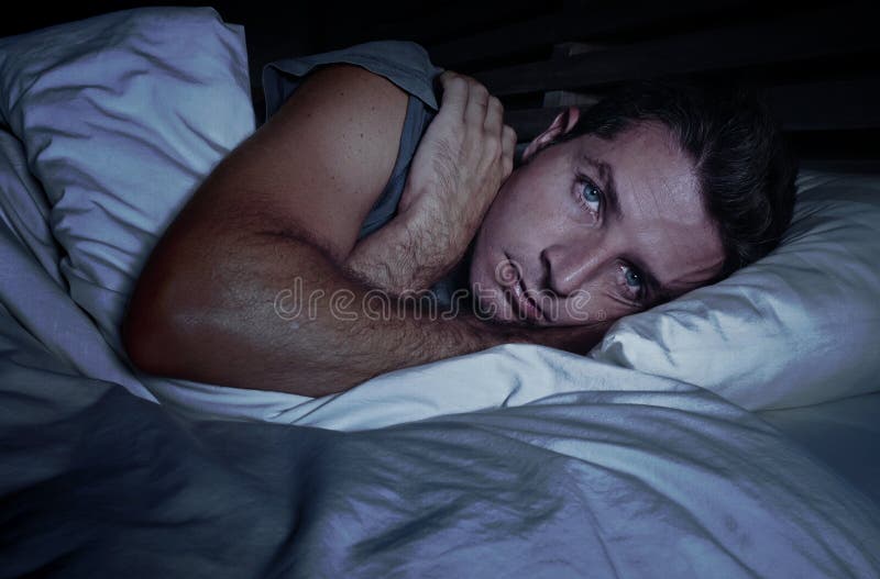 Homem atrativo novo preocupado agitado acordado na noite que encontra-se na cama sem sono com o diso de sofrimento aberto largo d imagens de stock Homem atrativo novo preocupado agitado acordado na noite que encontra-se na cama sem sono com o diso de sofrimento aberto largo d imagens de stock