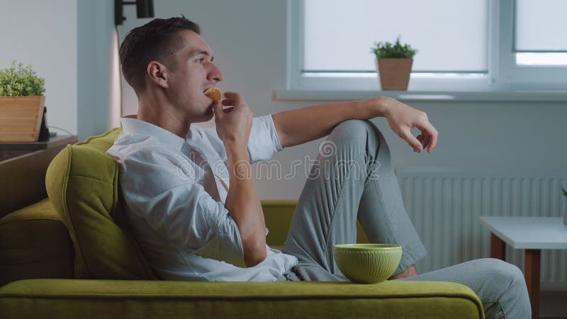 Jovem macho comendo batata frita assistindo filme na superfície branca