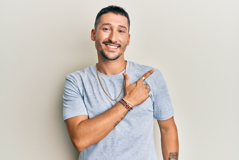 Handsome man with tattoos wearing casual 90s style and gold chain smiling cheerful pointing with hand and finger up to the side. Handsome man with tattoos wearing casual 90s style and gold chain smiling cheerful pointing with hand and finger up to the side