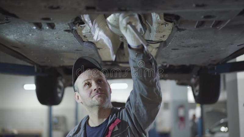 Homem caucasiano adulto limpando a testa com a mão enquanto apertava os parafusos no fundo do carro. retrato do automóvel masculin