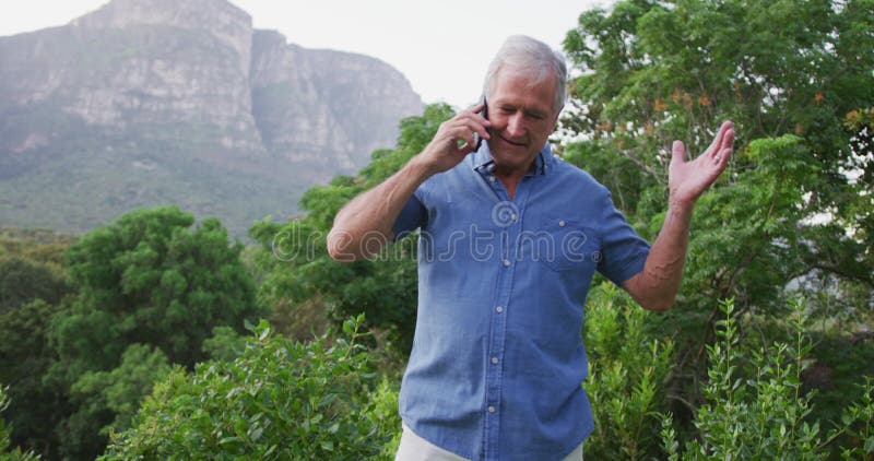 Homem caucasiano sênior sorrindo e falando ao telefone no jardim