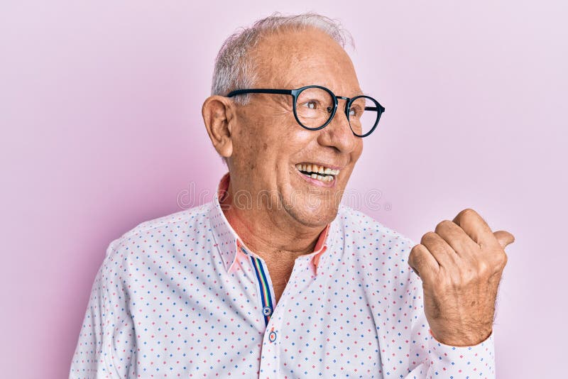 Senior caucasian man wearing casual clothes and glasses pointing thumb up to the side smiling happy with open mouth. Senior caucasian man wearing casual clothes and glasses pointing thumb up to the side smiling happy with open mouth