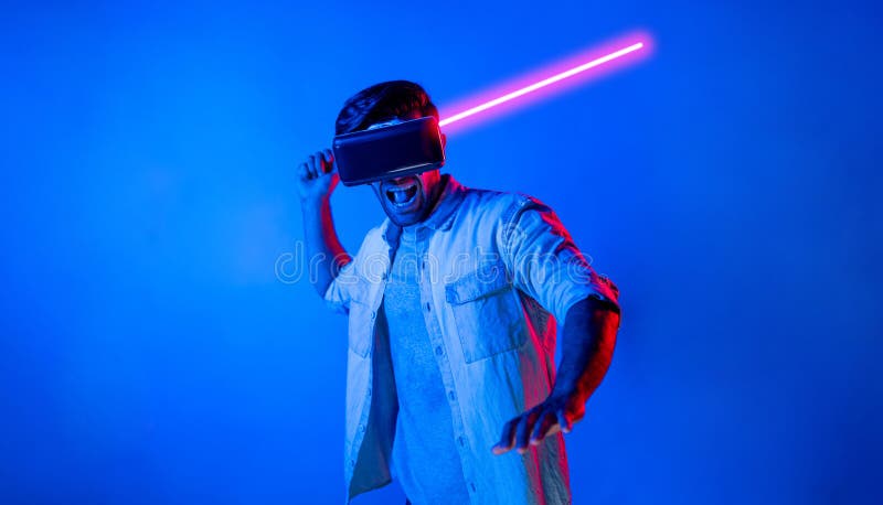 Caucasian man wearing VR glass and moving gesture holding sword. Gamer using future digital virtual reality headset or futuristic innovation to enter meta world or playing action game. Deviation. Caucasian man wearing VR glass and moving gesture holding sword. Gamer using future digital virtual reality headset or futuristic innovation to enter meta world or playing action game. Deviation.