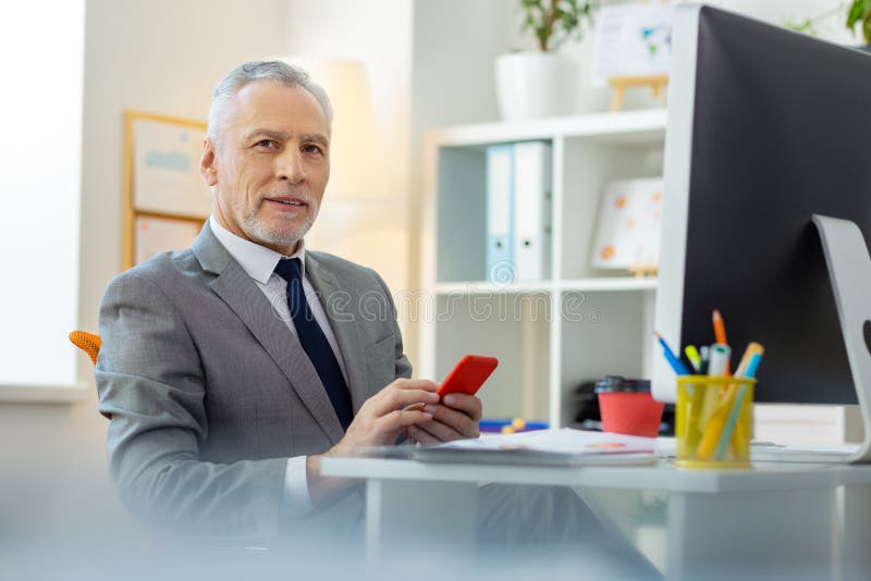 Homem cinzento-de cabelo sério com os olhos escuros que levam o smartphone vermelho imagem de stock royalty free Homem cinzento-de cabelo sério com os olhos escuros que levam o smartphone vermelho imagem de stock royalty free