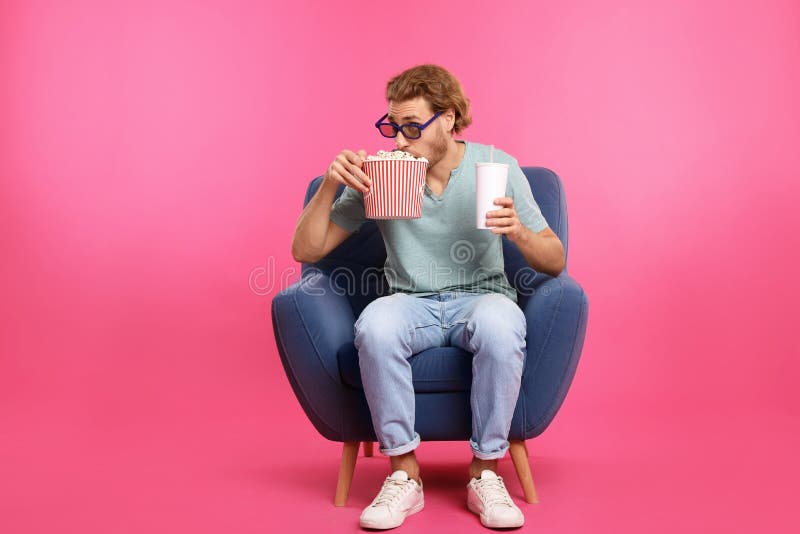 Homem com os vidros 3D, a pipoca e a bebida sentando-se na poltrona durante a mostra do cinema imagens de stock royalty free Homem com os vidros 3D, a pipoca e a bebida sentando-se na poltrona durante a mostra do cinema imagens de stock royalty free