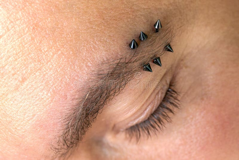 Homem com piercing na sobrancelha. três pequenos piercings pretos.