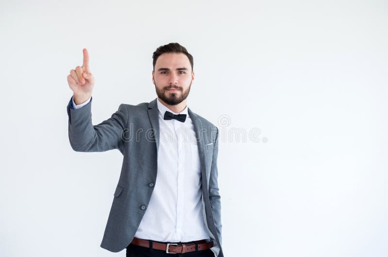 Homem considerável com o farpado no smoking e na mão formais da exibição do terno que aponta no fundo branco imagem de stock Homem considerável com o farpado no smoking e na mão formais da exibição do terno que aponta no fundo branco imagem de stock