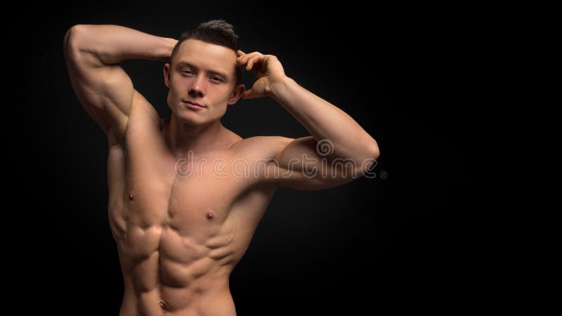 Homem considerável da forma com corpo muscular Close up do abdômen do ` s do homem novo do ajuste contra o fundo escuro fotografia de stock royalty free Homem considerável da forma com corpo muscular Close up do abdômen do ` s do homem novo do ajuste contra o fundo escuro fotografia de stock royalty free