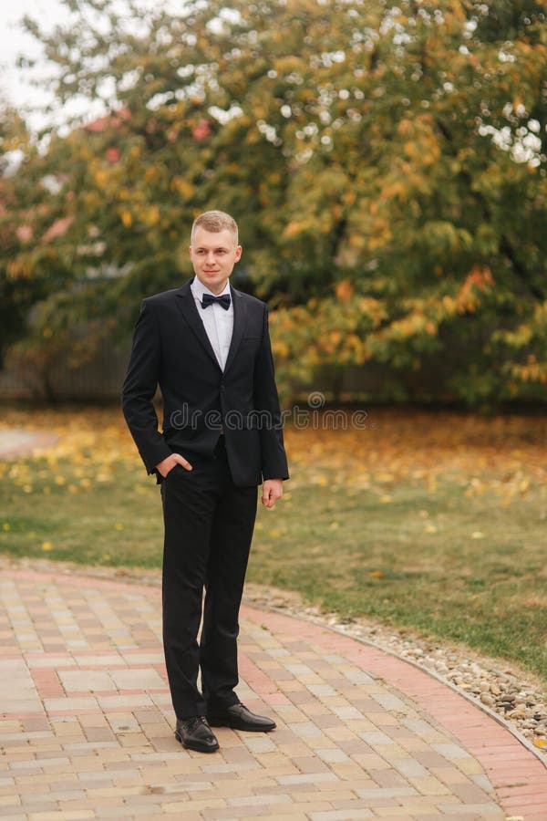 Homem considerável na posição preta do terno exterior no outono Noiva de espera do noivo fotografia de stock Homem considerável na posição preta do terno exterior no outono Noiva de espera do noivo fotografia de stock