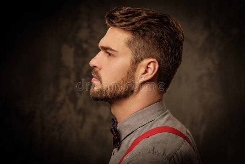 Homem considerável novo com os suspensórios vestindo da barba e levantamento no fundo escuro imagem de stock Homem considerável novo com os suspensórios vestindo da barba e levantamento no fundo escuro imagem de stock