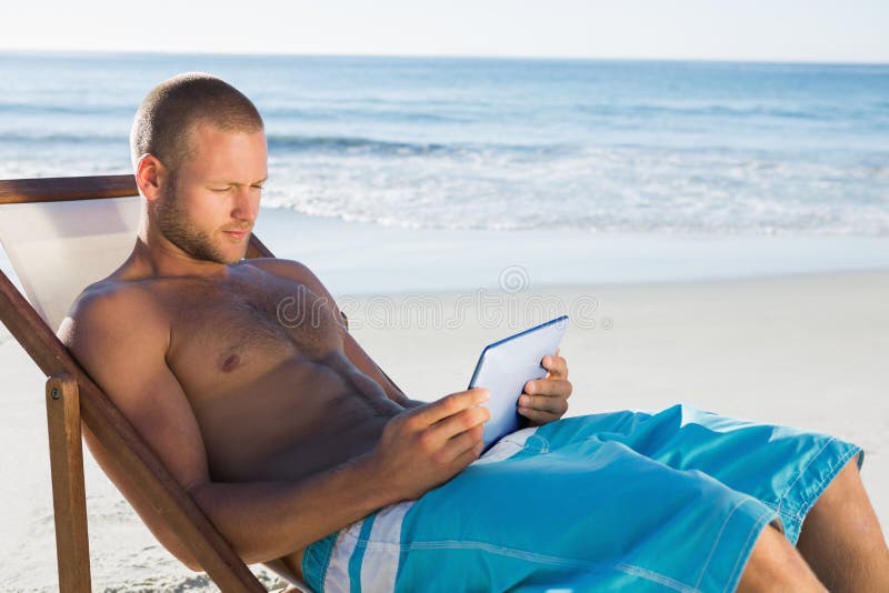 Homem considerável que usa sua tabuleta ao tomar sol foto de stock Homem considerável que usa sua tabuleta ao tomar sol foto de stock
