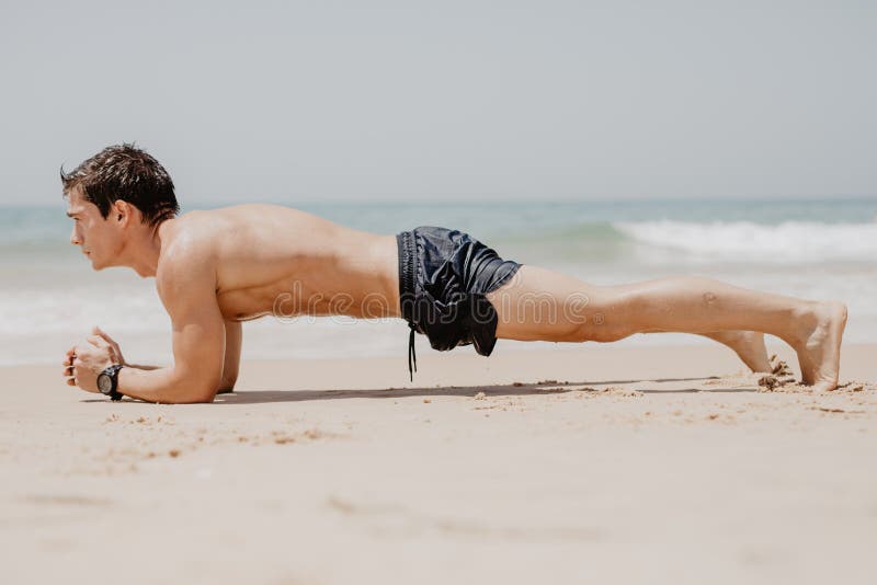 Homem da aptidão que faz o exercício da flexão de braço na praia O retrato do indivíduo do ajuste que dá certo seu núcleo dos mús