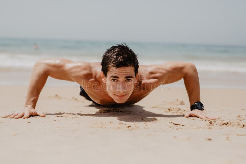 Homem da aptidão que faz o exercício da flexão de braço na praia O retrato do indivíduo do ajuste que dá certo seu núcleo dos mús