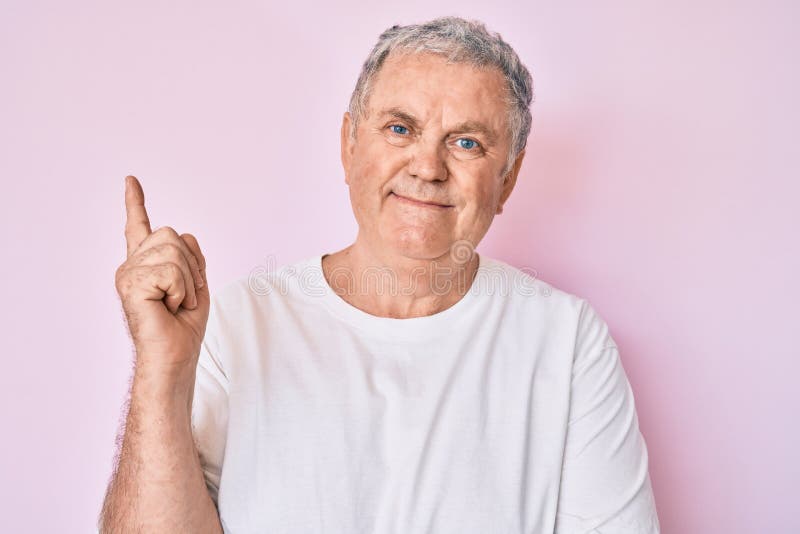 Senior grey-haired man wearing casual white tshirt smiling happy pointing with hand and finger to the side. Senior grey-haired man wearing casual white tshirt smiling happy pointing with hand and finger to the side