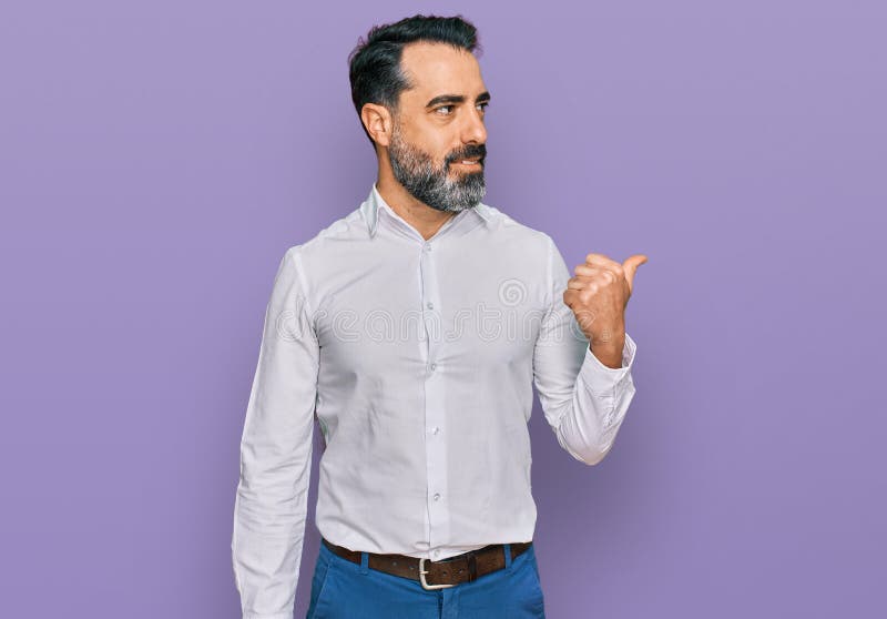 Middle aged man with beard wearing casual white shirt smiling with happy face looking and pointing to the side with thumb up. Middle aged man with beard wearing casual white shirt smiling with happy face looking and pointing to the side with thumb up