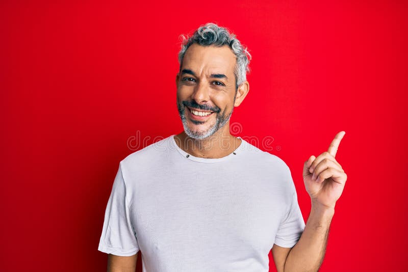 Middle age grey-haired man wearing casual white tshirt smiling happy pointing with hand and finger to the side. Middle age grey-haired man wearing casual white tshirt smiling happy pointing with hand and finger to the side