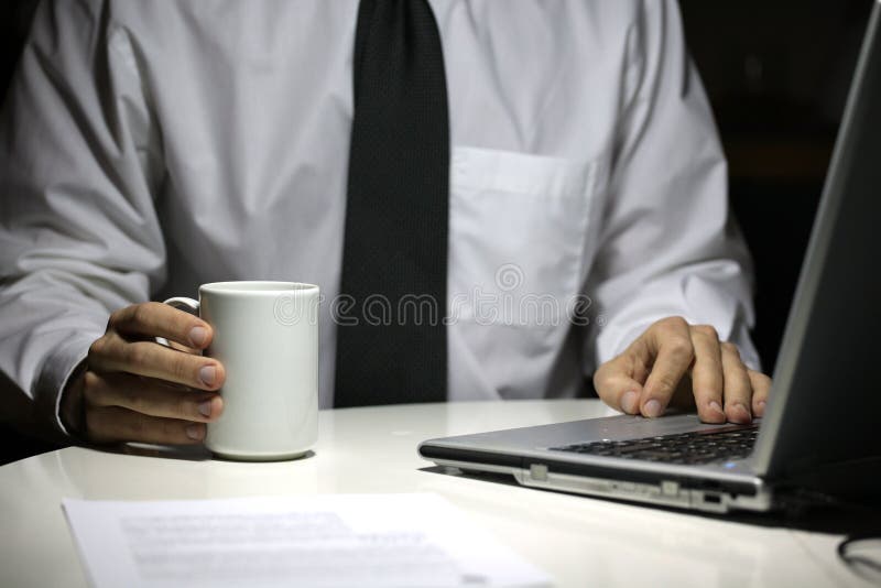 Homem de negócio com o copo de café que trabalha no portátil