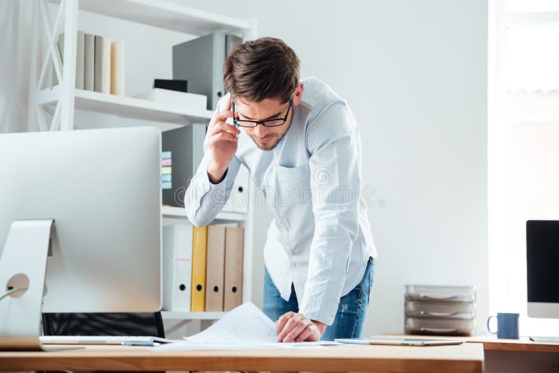 Homem de negócio que está na mesa que trabalha em originais com telefone celular fotos de stock Homem de negócio que está na mesa que trabalha em originais com telefone celular fotos de stock