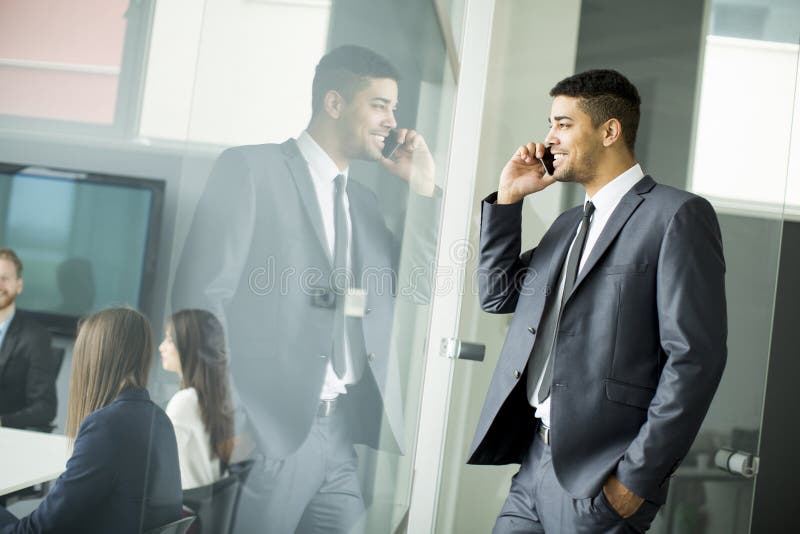Homem de negócios africano novo que usa o telefone celular em seu escritório imagem de stock royalty free Homem de negócios africano novo que usa o telefone celular em seu escritório imagem de stock royalty free