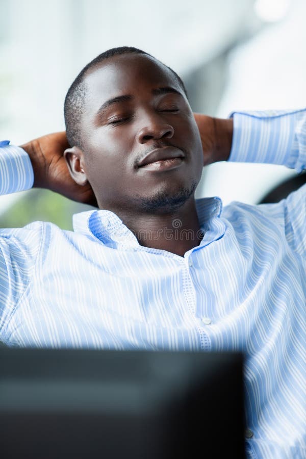 Homem de negócios afro-americano na camisa azul que relaxa no escritório após o dia de trabalho duro fotografia de stock Homem de negócios afro-americano na camisa azul que relaxa no escritório após o dia de trabalho duro fotografia de stock