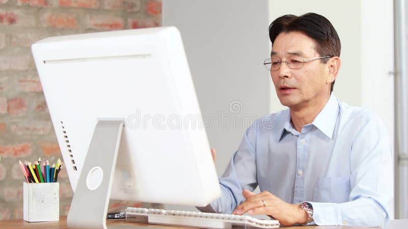Homem de negócios asiático que usa o computador na mesa