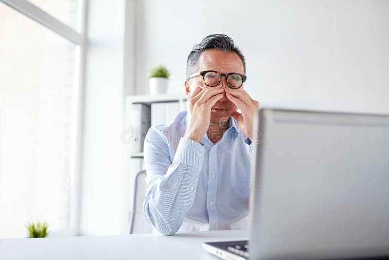 Homem de negócios cansado nos vidros com o portátil no escritório foto de stock Homem de negócios cansado nos vidros com o portátil no escritório foto de stock