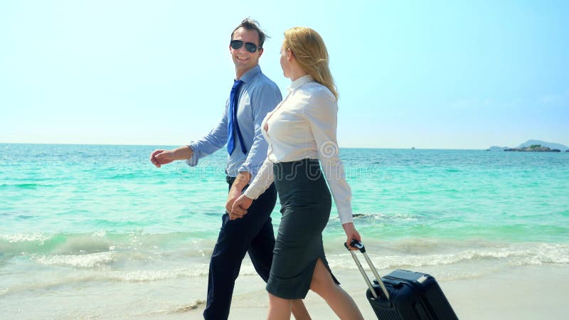Homem de negócios e mulher de negócio com uma mala de viagem que anda ao longo da praia branca da areia na ilha foto de stock royalty free Homem de negócios e mulher de negócio com uma mala de viagem que anda ao longo da praia branca da areia na ilha foto de stock royalty free