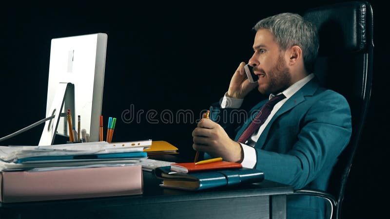 Homem de negócios farpado irritado que tem a conversação fatigante emocional em seu telefone celular Fundo preto foto de stock Homem de negócios farpado irritado que tem a conversação fatigante emocional em seu telefone celular Fundo preto foto de stock